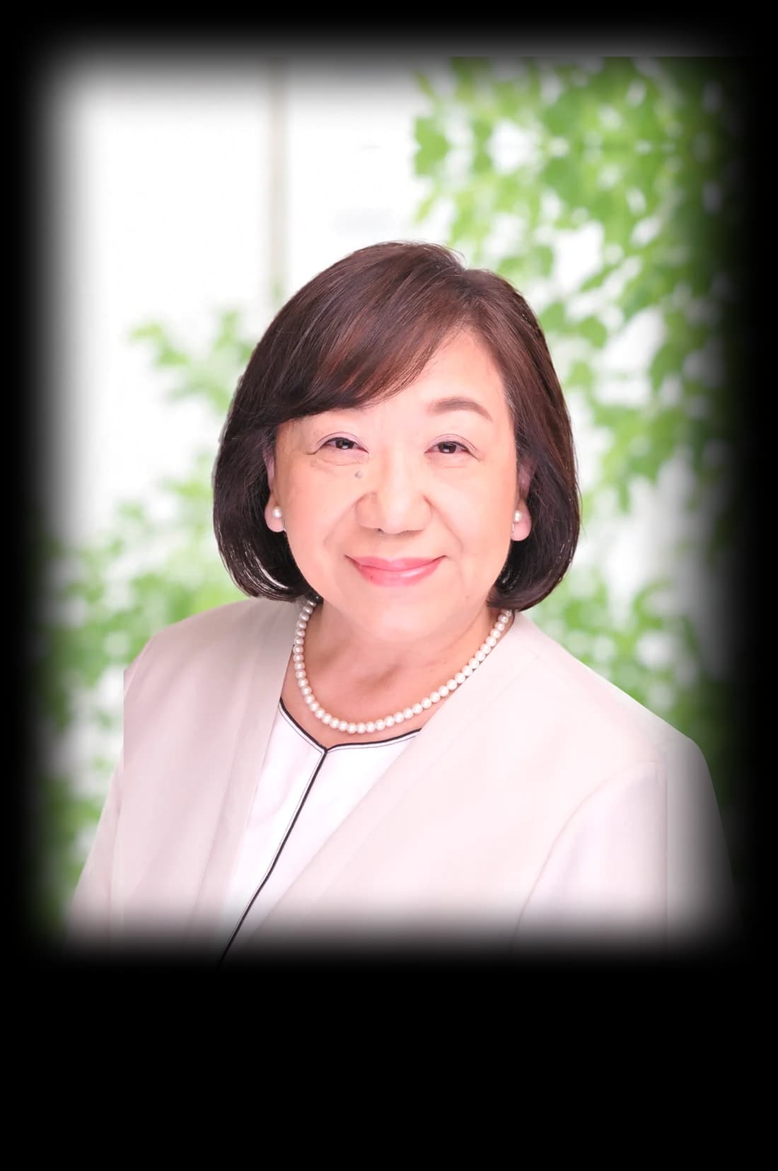 清田のり子の写真。やわらかい緑を背景に、白い上着と真珠のネックレスでほほえんでいる
