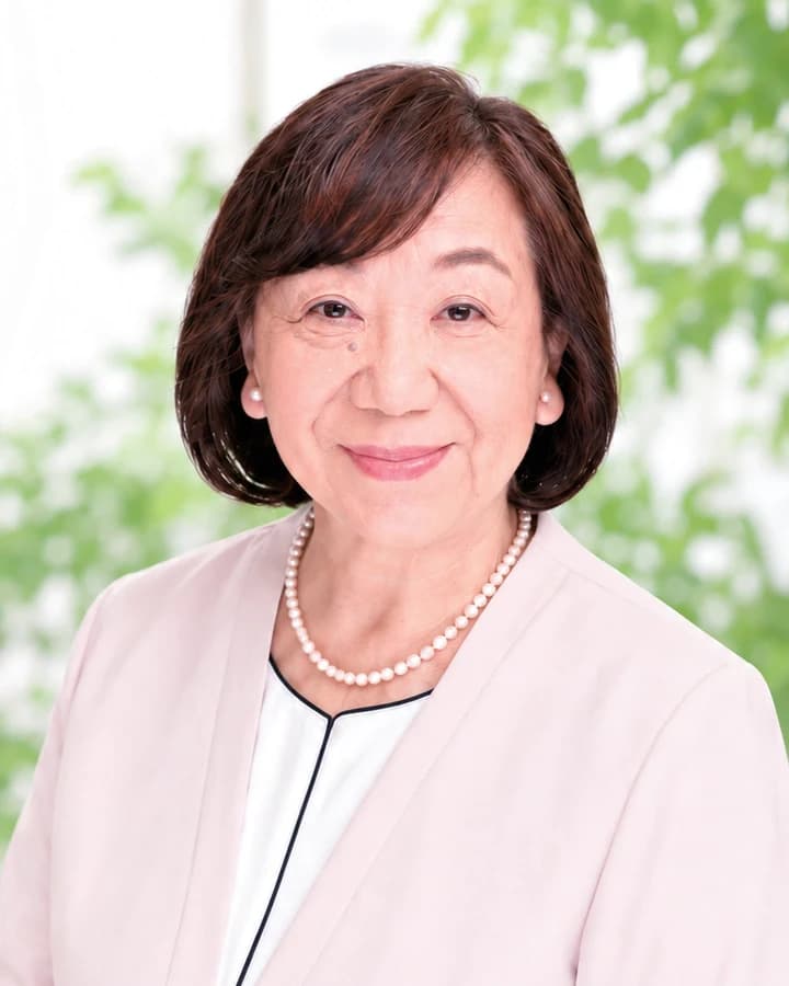 清田のり子の写真。やわらかい緑の窓辺で、白い上着に真珠のネックレスでほほえんでいる